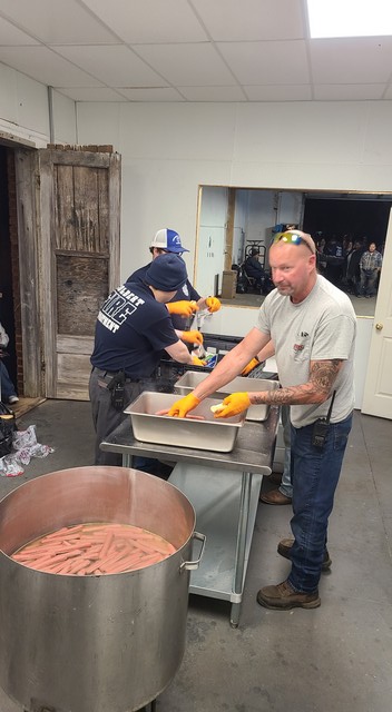 LOCAL VOLUNTEER FIRE FIGHTERS ASSIST IN COOKING AND SERVING HOTDOGS.